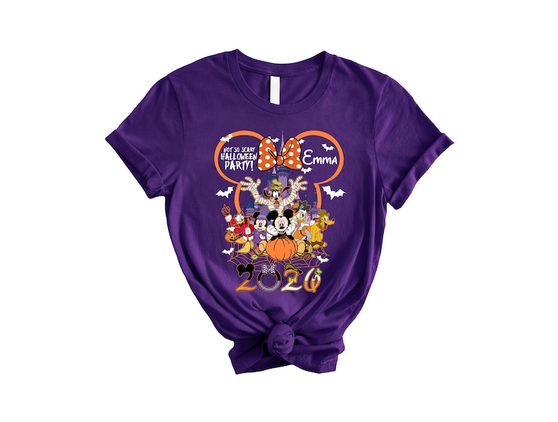 May include: A purple short-sleeve t-shirt featuring a graphic of Disney characters in Halloween costumes, a castle, and the text "Not So Scary Halloween Party!", "Emma", and "2020". The design includes a large orange Mickey Mouse ear outline.