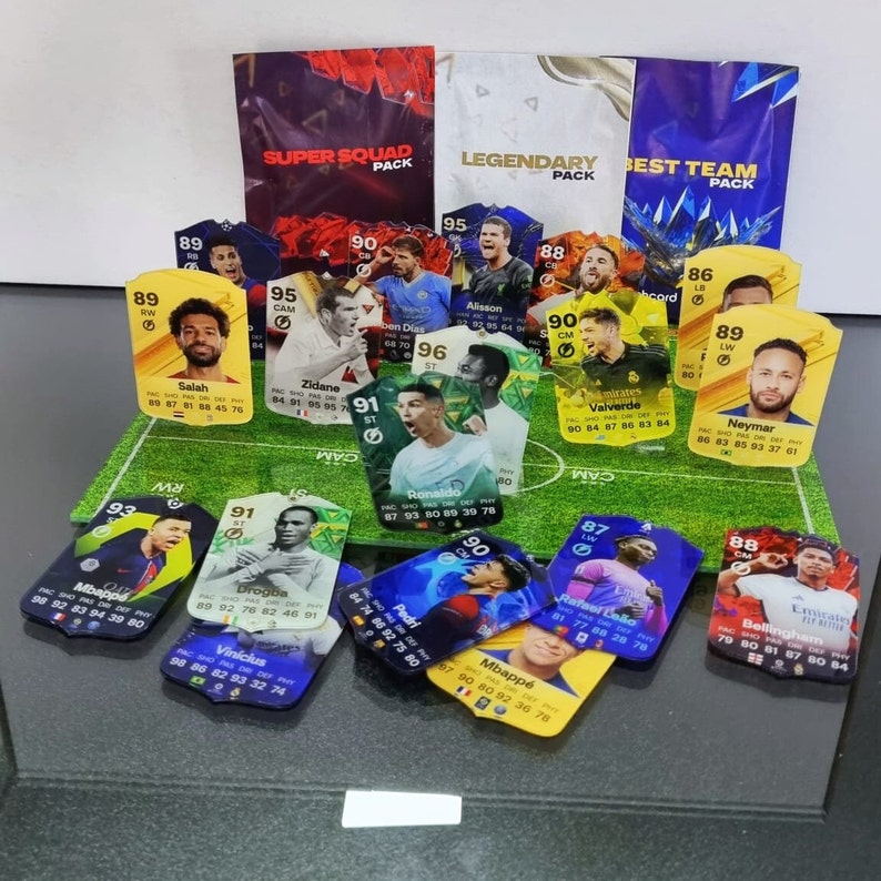 May include: A collection of colorful trading cards featuring various soccer players. The cards are arranged on a green artificial turf surface. The cards feature player names, ratings, and statistics. The cards are from the Super Squad, Legendary, and Best Team packs.