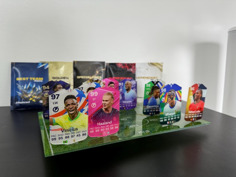 May include: A collection of colorful trading cards featuring soccer players. The cards are displayed on a green field background. The cards feature the players' names, ratings, and statistics. The cards are from the game FIFA.