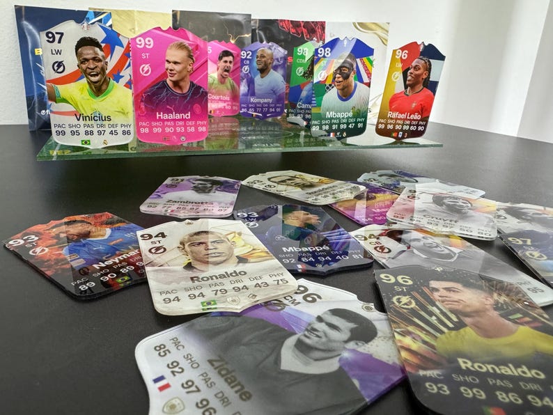 May include: A collection of colorful trading cards featuring various soccer players. The cards are made of plastic and have a glossy finish. The cards feature the players' names, team logos, and statistics. The cards are arranged in a random order on a table.
