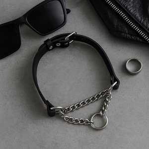 Black leather choker with metal chains and O-ring styled with sunglasses and ring – gothic punk flat lay.