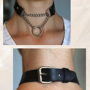May include: A black leather choker with a silver chain and a large silver ring. The choker has a buckle closure.