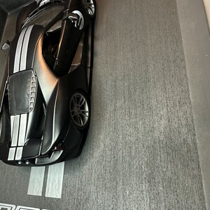 May include: A black Ford GT model car with white racing stripes. The model has the number "2" on the hood and doors. The car is displayed in a black box with the Ford GT logo and "66 Le Mans Heritage" text.