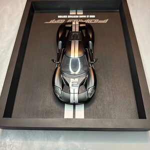 May include: A black and silver Ford GT model car, displayed in a black tray. The car has white racing stripes and the number 2 on the hood. The tray has the text "1966 Le Mans Heritage Edition" and "Ford GT".