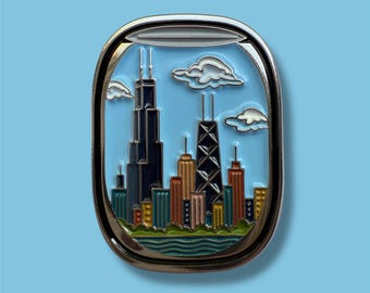 May include: A metal pin featuring a stylized Chicago skyline viewed through a window frame. The pin showcases the city's iconic skyscrapers against a light blue sky with fluffy white clouds. The pin has a silver border.