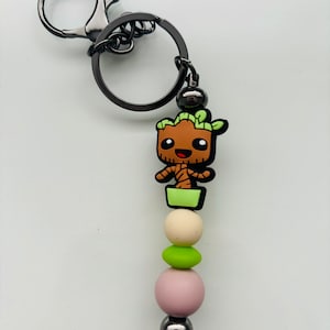 May include: A black metal keychain with a green, brown, and white silicone Groot character charm and a string of colourful silicone beads.