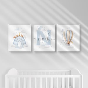 May include: Set of three framed nursery art prints. The prints feature a blue rainbow with animal figures, the name "Noah" in script, and a hot air balloon with a giraffe. The art has a watercolor style with soft colors.