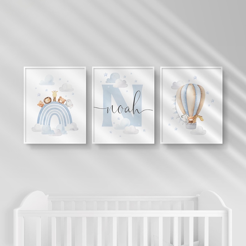 May include: Set of three framed nursery art prints. The prints feature a blue rainbow with animal figures, the name "Noah" in script, and a hot air balloon with a giraffe. The art has a watercolor style with soft colors.