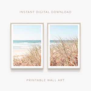 Op de afbeelding: Twee ingelijste prints met een strandscène. De prints tonen een zandstrand, oceaangolven en een blauwe lucht. Hoge, gedroogde grassen staan op de voorgrond. De tekst "INSTANT DIGITAL DOWNLOAD" en "PRINTABLE WALL ART" zijn zichtbaar.