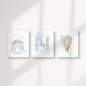 May include: Three framed watercolor prints with a nursery theme. One print features a rainbow with animals, another has the name "Noah" with a large "N", and the third shows a hot air balloon with a giraffe.