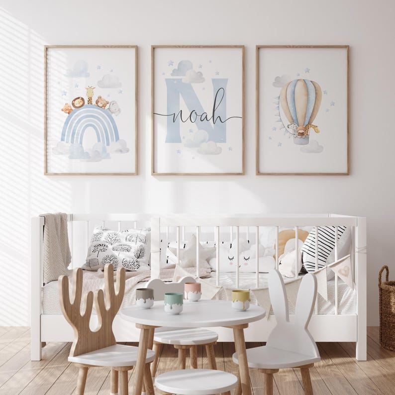 May include: Three framed nursery art prints. One features a rainbow with animals, another has the name "Noah" with clouds, and the third shows a hot air balloon. The room also includes a white crib, a small table, and unique chairs.