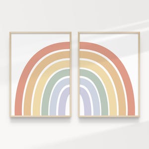 May include: Two framed art prints with a rainbow design. Each print shows a semi-circular rainbow with bands of red, orange, yellow, green, and blue. The artwork is set against a white background, framed in light wood.