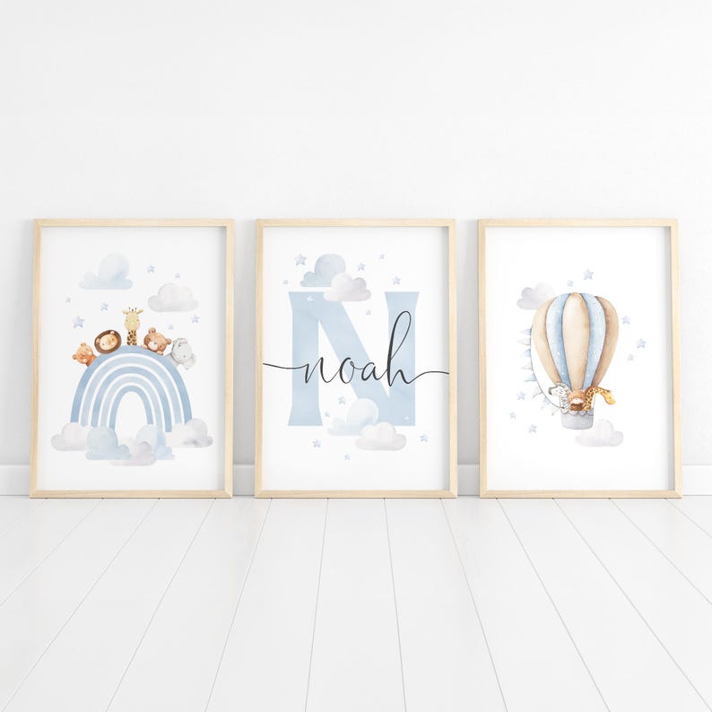 May include: Three framed art prints with a nursery theme. The prints feature a rainbow with animals, the name "Noah" with a blue "N", and a hot air balloon with a giraffe. The color palette includes blue, beige, and white.