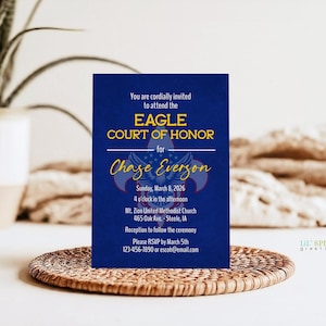 May include: A navy blue invitation card for an Eagle Court of Honor, featuring gold text and a scout emblem. The card includes details for Chase Everson's ceremony, date, time, and location. It rests on a woven, circular placemat.
