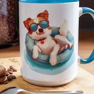 May include: White ceramic mug with a blue rim and handle. The mug features a cartoon illustration of a dog wearing sunglasses and relaxing in a blue inflatable pool ring.
