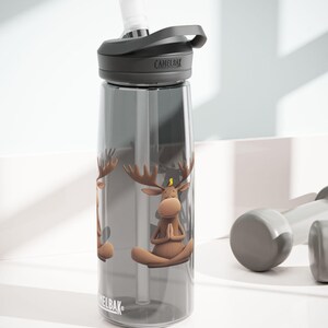 Könnte beinhalten: Eine graue Wasserflasche mit schwarzem Deckel und Strohhalm. Die Flasche hat ein Motiv eines Yoga machenden Elchs mit einem Vogel auf dem Kopf. Die Flasche ist mit "CamelBak" beschriftet.