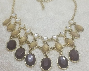May include: A gold chain necklace with a multi-tiered design featuring brown, beige, and clear oval-shaped stones.