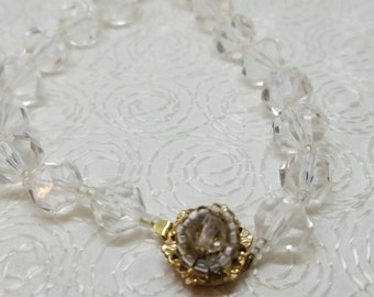 May include: A clear crystal necklace with a gold clasp. The necklace is made of faceted beads and has a delicate, elegant look.