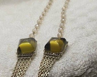 May include: A gold necklace with a beaded chain and two square-shaped pendants with yellow and black glass stones.