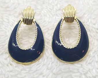 May include: A pair of gold-tone earrings with a blue enamel finish. The earrings are shaped like a teardrop with a circular opening in the center.