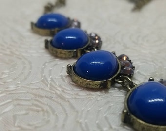 May include: A blue and gold necklace with four oval-shaped blue stones and small clear rhinestones.