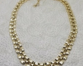 May include: A gold-tone chain necklace with a textured, box-link design. The necklace is made of metal and has a simple, elegant style.