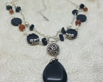 May include: A silver chain necklace with black and brown beads, a silver pendant with a circle design, and a large black teardrop-shaped pendant.