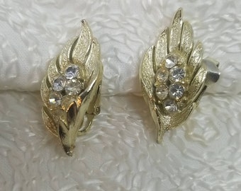May include: A pair of gold tone clip-on earrings with a leaf design and clear rhinestones.