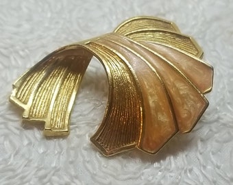 May include: A gold-toned brooch with a fan-shaped design. The brooch is made of metal and has a pink enamel finish.