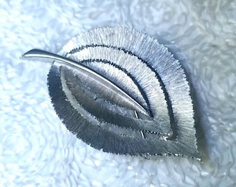 May include: A silver leaf-shaped brooch with a textured, layered design.