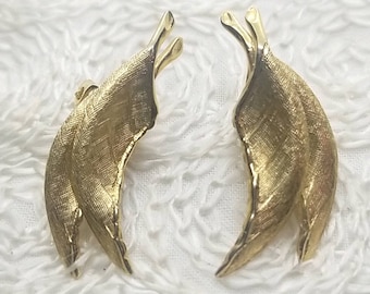 May include: A pair of gold-tone earrings shaped like leaves. The leaves are textured and have a slightly curved shape.