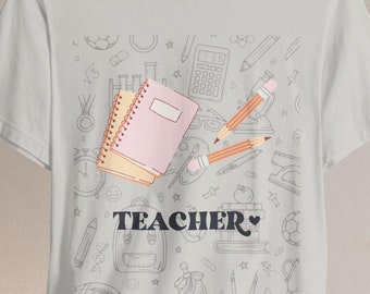 May include: A white t-shirt featuring a black and white illustration of school supplies, including pencils, notebooks, a calculator, and a backpack. The text "TEACHER" is printed in black with a heart symbol.