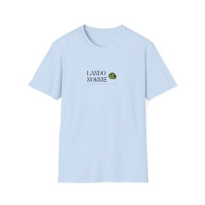 May include: Light blue t-shirt with a black and white graphic of Lando Norris's McLaren Formula 1 Team logo.