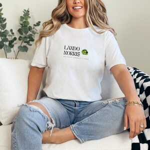 May include: A white t-shirt with a black graphic print that says "Lando Norris McLaren Formula 1 Team" with a green and black logo.