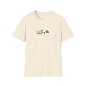 May include: A cream coloured t-shirt with a black and green graphic print that says "LANDO NORRIS McLaren Formula 1 Team".