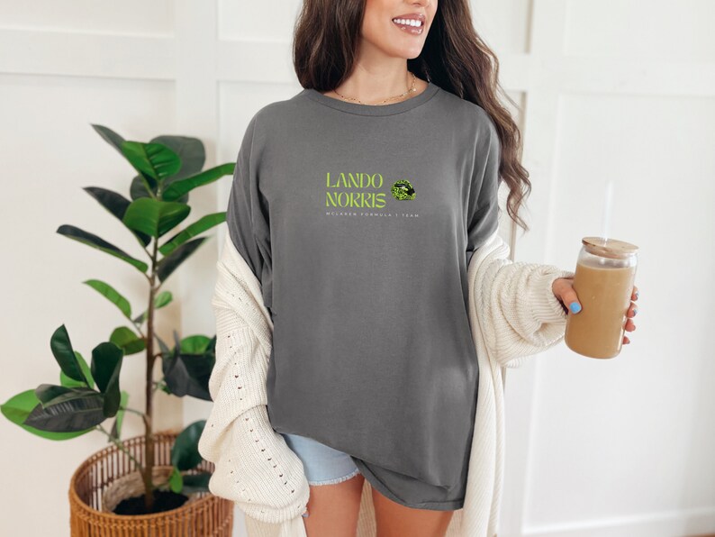 May include: A grey long-sleeved t-shirt with the text "Lando Norris McLaren Formula 1 Team" and a green and black graphic of a lip print.