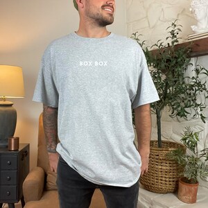 May include: A heather grey t-shirt with the text "BOX BOX" printed in white on the front.