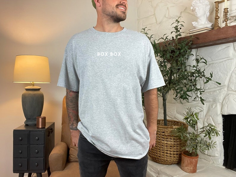 May include: A heather grey t-shirt with the text "BOX BOX" printed in white on the front.