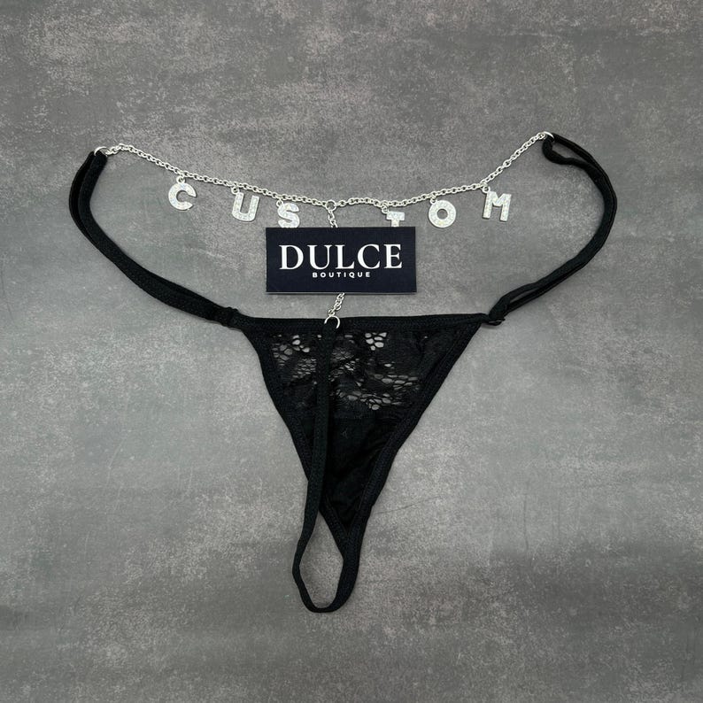 Puede incluir: Lingerie de encaje negro con una cadena plateada y abalorios que deletrean "CUSTOM". La cadena est&aacute; unida a la parte delantera de la lencer&iacute;a y tiene una etiqueta que dice "DULCE BOUTIQUE".