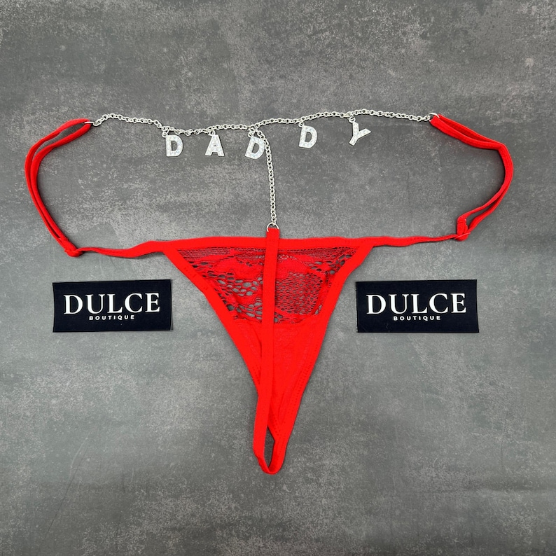 Puede incluir: Lingerie de encaje roja con una cadena plateada con la palabra "DADDY" escrita en pedrer&iacute;a.