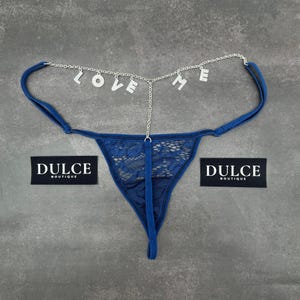 Puede incluir: Lingerie de encaje azul con una cadena plateada con la palabra "LOVE ME" colgando de ella. La lencer&iacute;a tiene una etiqueta que dice "Dulce Boutique".