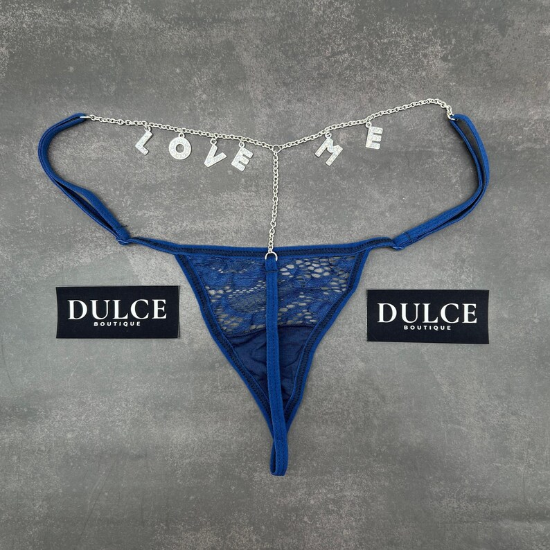 Puede incluir: Lingerie de encaje azul con una cadena plateada con la palabra "LOVE ME" colgando de ella. La lencer&iacute;a tiene una etiqueta que dice "Dulce Boutique".