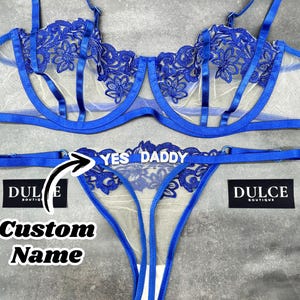 May include: A royal blue lingerie set featuring a sheer underwire bra with floral embroidery and matching thong underwear. The thong features the white text YES DADDY and an arrow pointing to the text with the words Custom Name below it.
