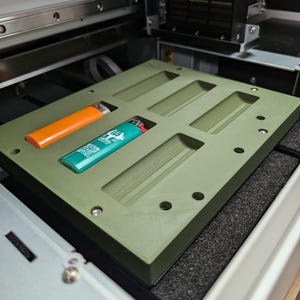 May include: A green plastic tray with multiple rectangular slots, designed to hold lighters. Two lighters are visible in the slots, one orange and one turquoise.