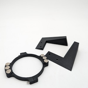 May include: A black 3D printed ring with five magnets attached to the outside. The ring is designed to hold a phone or other device. Two black 3D printed L-shaped brackets are also included.