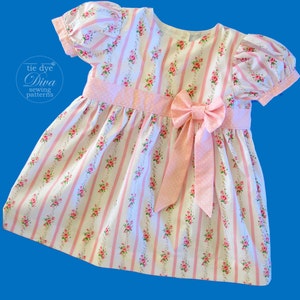 May include: A pink and white striped dress with a floral pattern and a pink bow. The dress has short puffed sleeves and a round neckline.