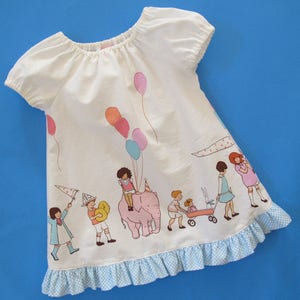 May include: White cotton dress with a ruffled hem and a print of children and balloons. The dress has short puffed sleeves and a scoop neck.
