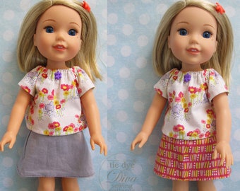 Op de afbeelding: Twee poppen die matchende bloemetjesprint tops dragen met korte mouwen en verschillende rokken. Eén pop draagt een paarse rok en de andere een roze en gele geruite rok. Beide poppen hebben blond haar en blauwe ogen.