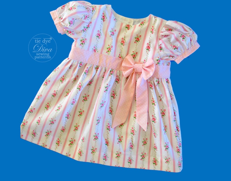 May include: A pink and white striped dress with a floral pattern and a pink bow. The dress has short puffed sleeves and a round neckline.
