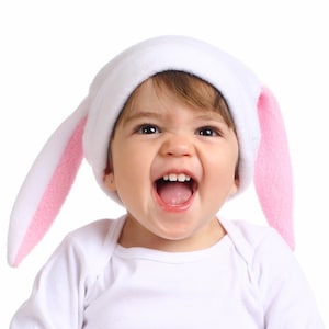 May include: A young child wearing a white bunny hat with pink ears, smiling and laughing with their mouth open.